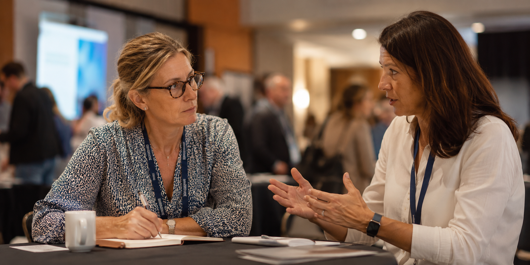 Two experienced professionals in conversation after a workshop, with one sharing expertise while the other takes notes, representing the trusted peer learning, professional discussion, and human insight that associations provide beyond information alone.