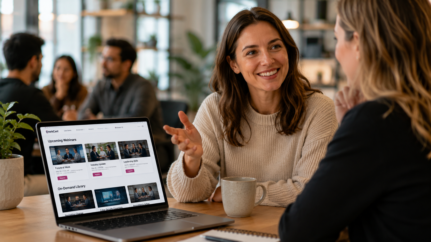 Two professionals having an engaging conversation in a modern networking space, smiling and sharing ideas while colleagues connect in the background, representing the meaningful relationships and positive experiences that encourage members to recommend an association to others.