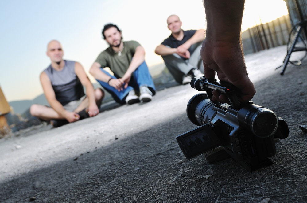 three men sitting on ground with a camera pointing at them